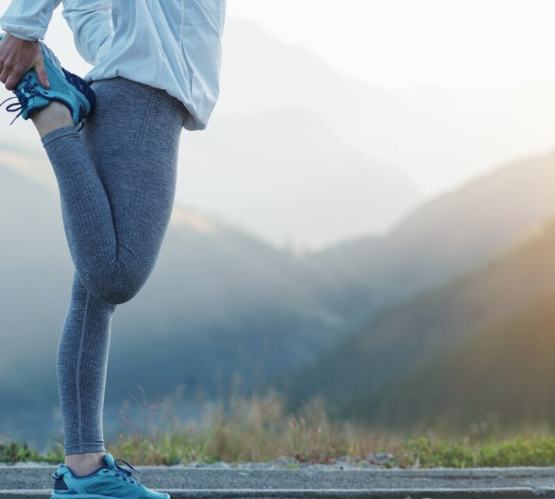 Runner stretching a leg on a mountain road at sunrise