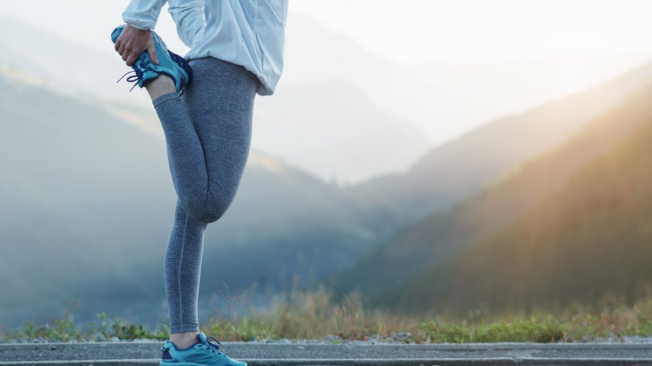 Runner stretching a leg on a mountain road at sunrise