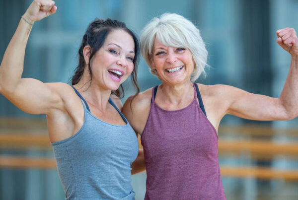 Two smiling women flexing their arm muscles