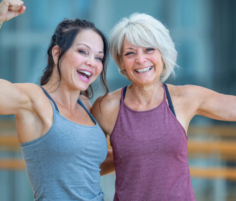 Two smiling women flexing their arm muscles